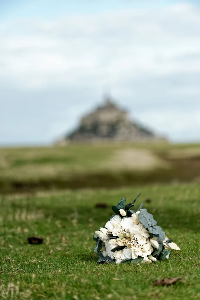 Bouquet de mariée fleurs blanches sur herbe, Mont Saint-Michel flou en arrière-plan, Normandie.