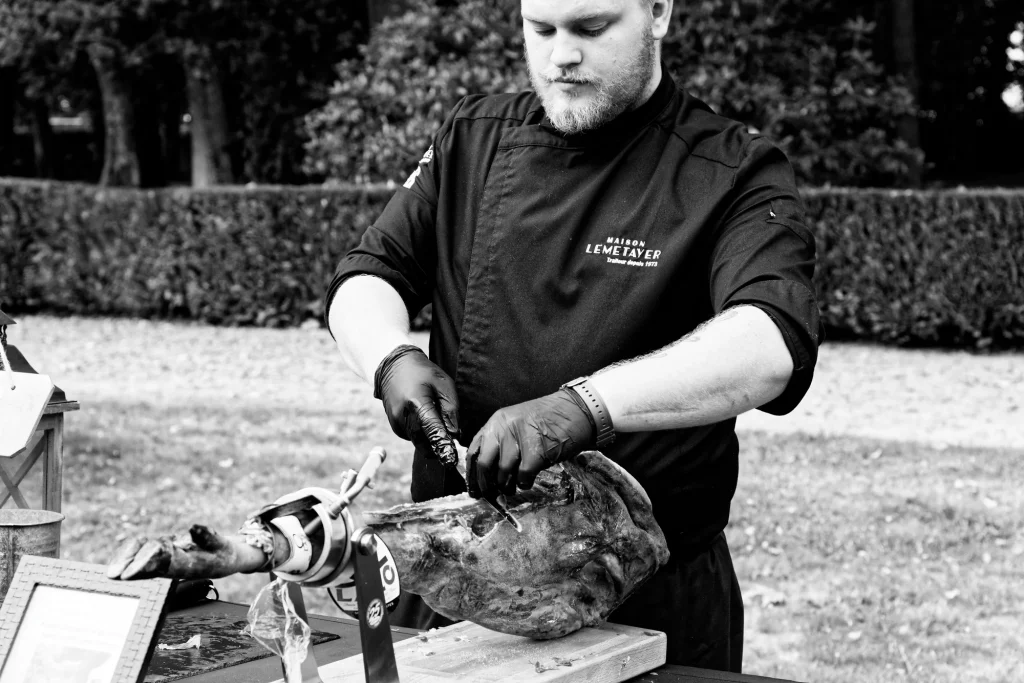Chef traiteur découpant un jambon à l'os pour un mariage en Normandie à Saint-Hilaire-du-Harcouët.