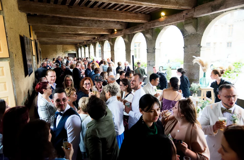 Cocktail de mariage sous les arches en pierre d'un domaine en Normandie, invités trinquant à l'Harcouët.