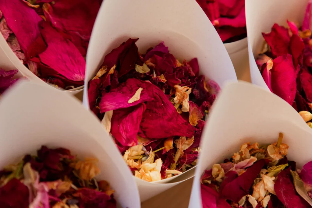 Cornets en papier blanc remplis de pétales de roses rouges et crème pour un mariage en Normandie.