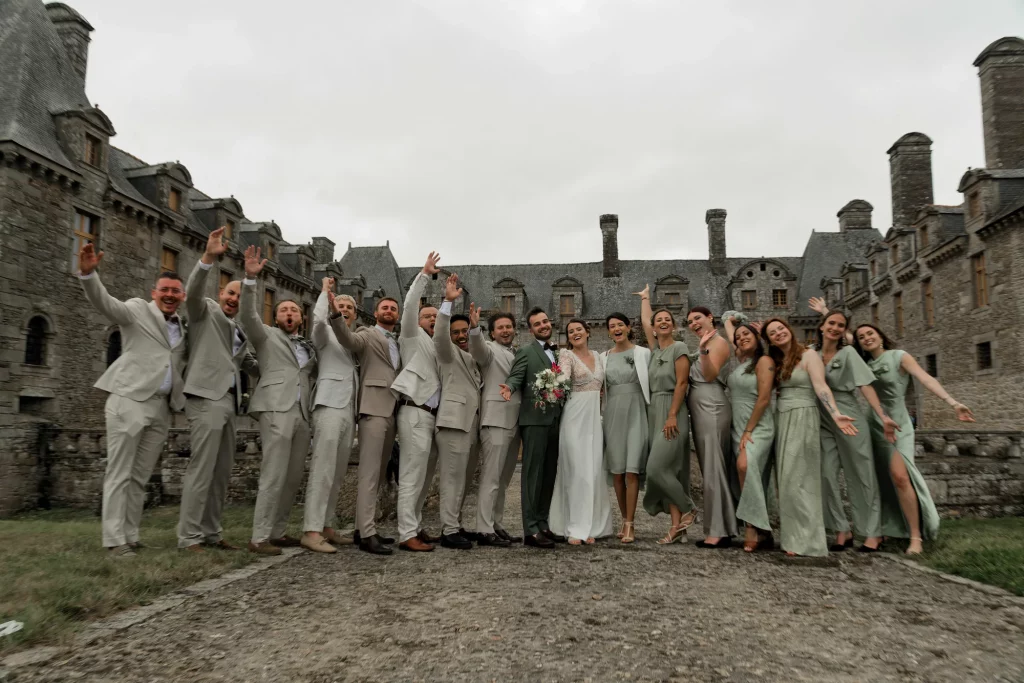 Cortège de mariage devant un château en Normandie, mariés et invités levant les bras à Saint-Hilaire-du-Harcouët.