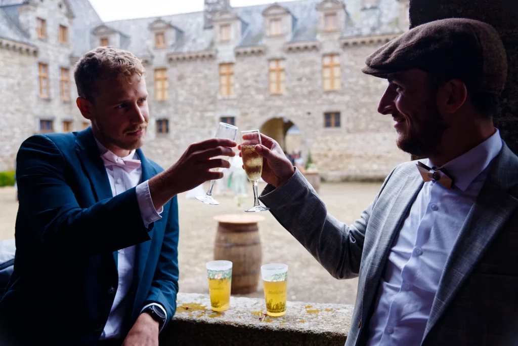 Deux hommes trinquent au champagne devant un château en pierre en Normandie lors d'un mariage.