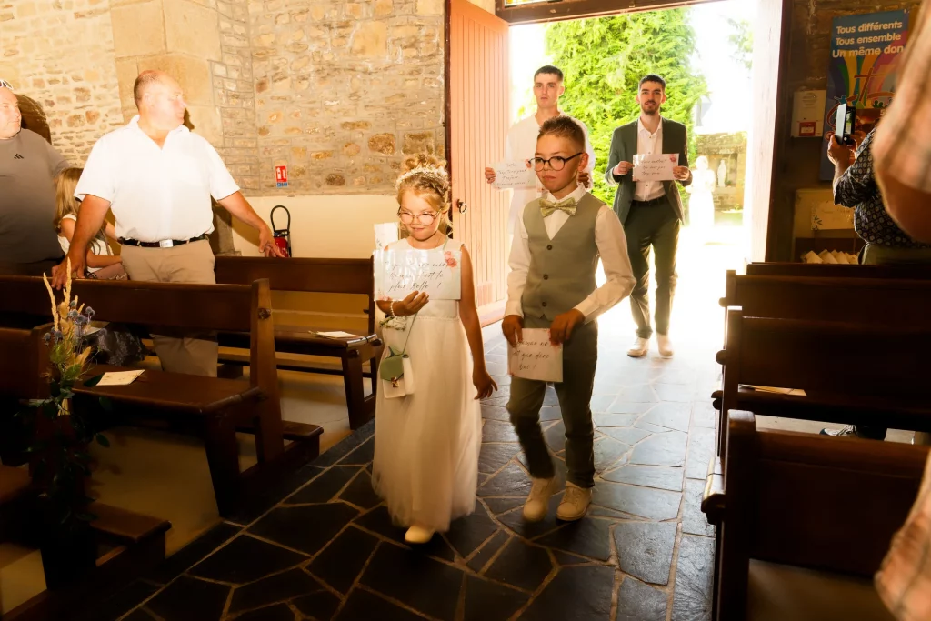 Enfants d'honneur avec pancartes entrant dans une église de Normandie à Saint-Hilaire-du-Harcouët.