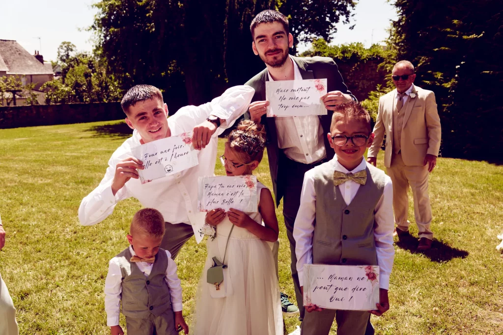 Enfants et témoins avec pancartes humoristiques lors d'un mariage à Saint-Hilaire-du-Harcouët en Normandie.