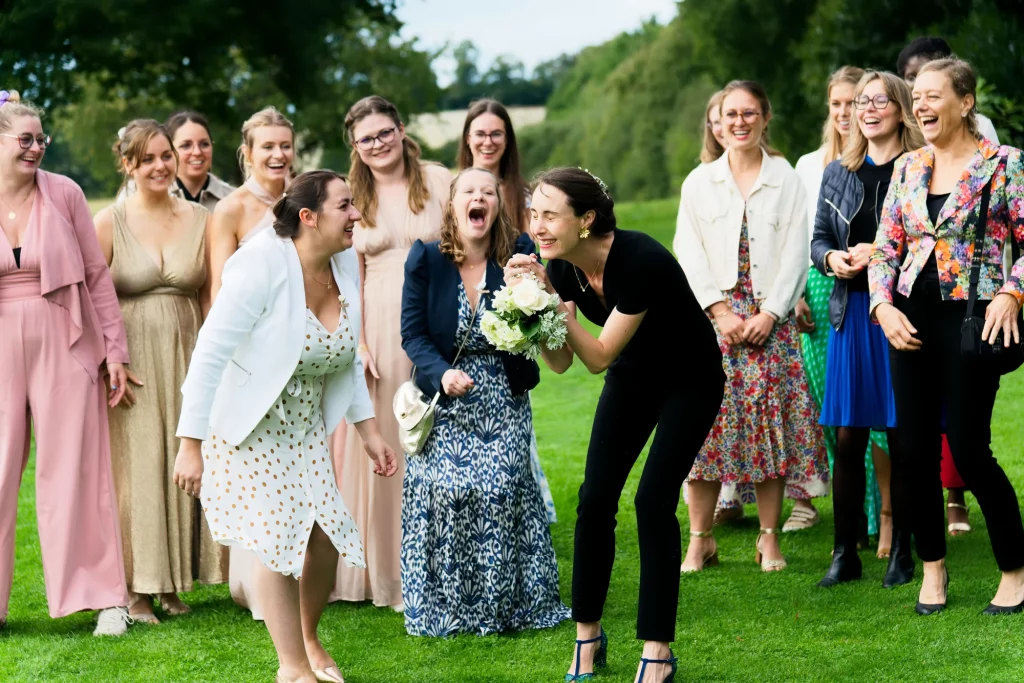 Femmes riant au lancer de bouquet en Normandie, une invitée en noir attrape les fleurs près d'Avranches.