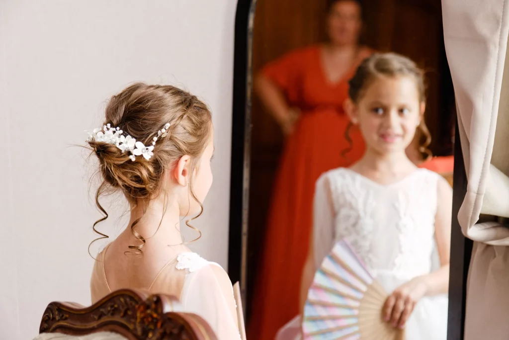 Fillette en robe blanche admirant sa coiffure fleurie dans un miroir lors d'un mariage en Normandie.