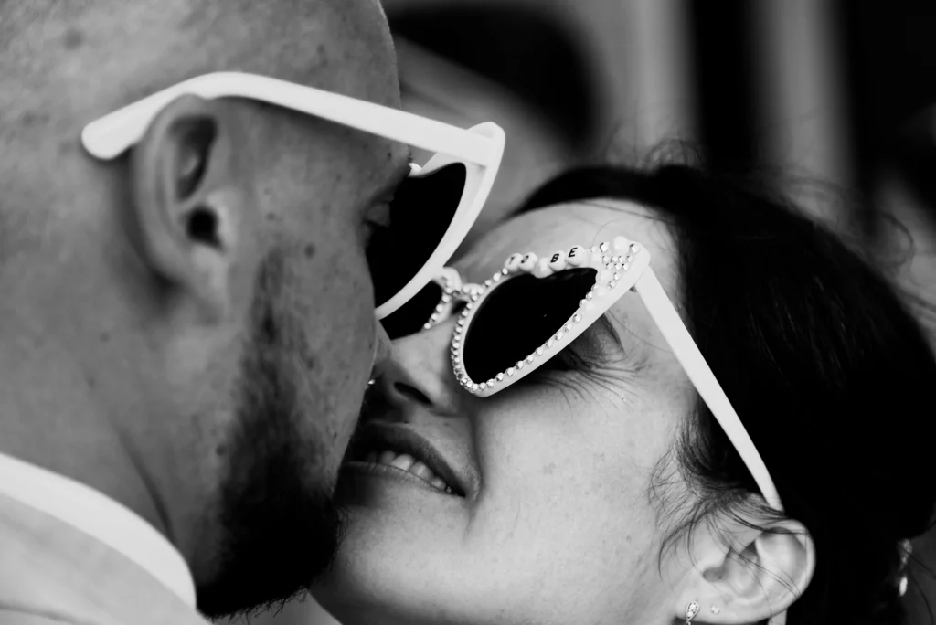 Gros plan en noir et blanc des mariés portant des lunettes de soleil en forme de cœur.