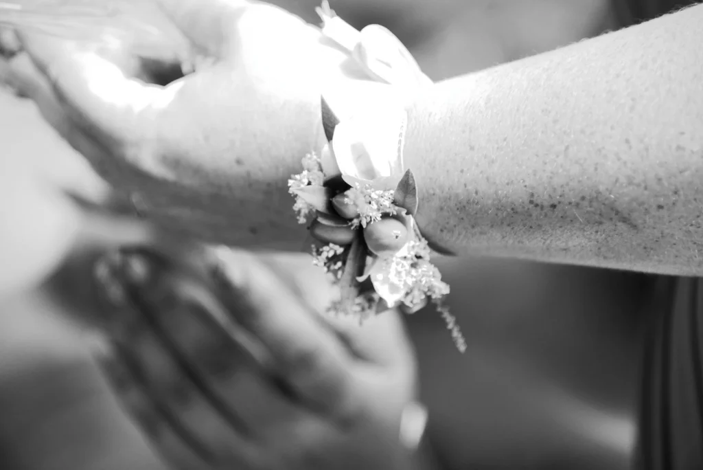 Gros plan noir et blanc d'un corsage fleuri au poignet d'une invitée de mariage en Normandie.