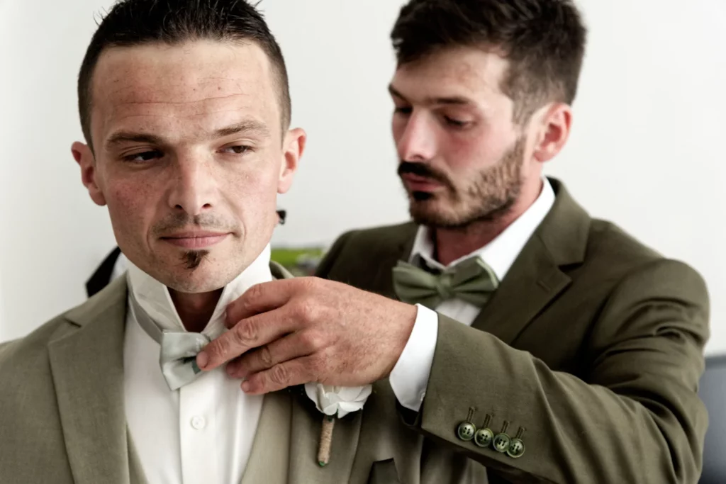 Homme ajustant le nœud papillon du marié, préparatifs de mariage en Normandie à Saint-Hilaire-du-Harcouët.