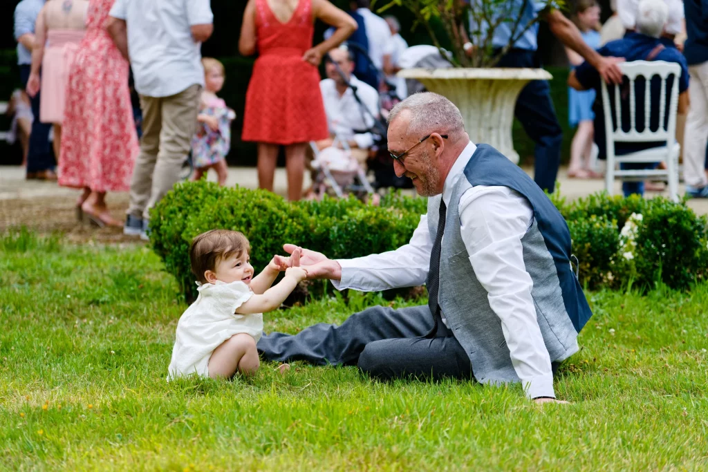 Homme jouant avec un bébé sur l'herbe lors d'un mariage en Normandie à Saint-Hilaire-du-Harcouët.