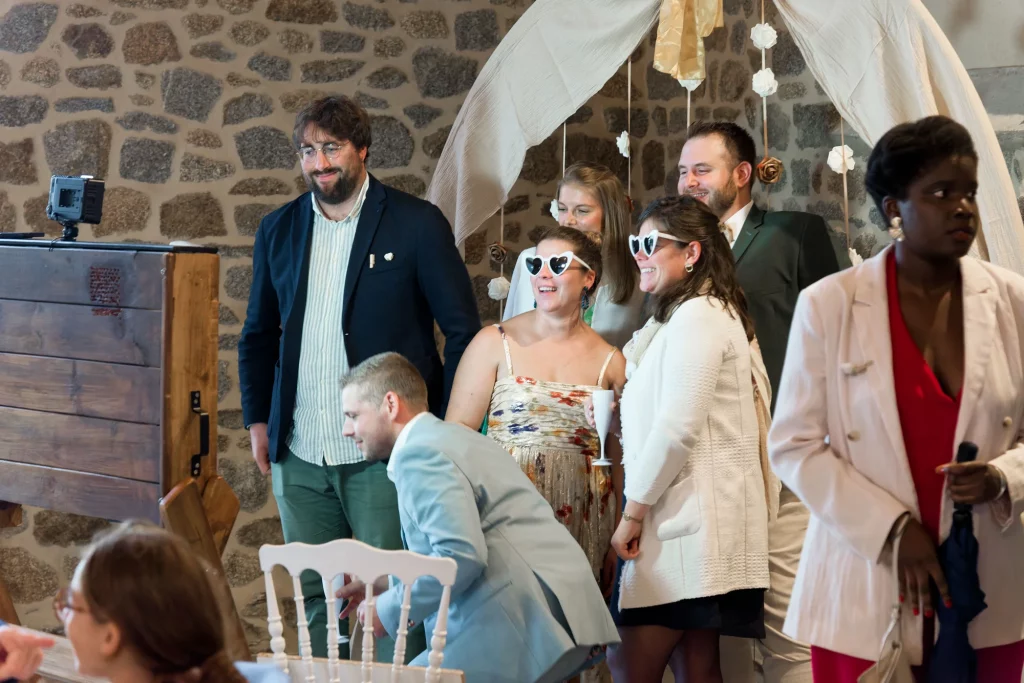 Invités de mariage avec lunettes cœur devant un mur en pierre en Normandie.