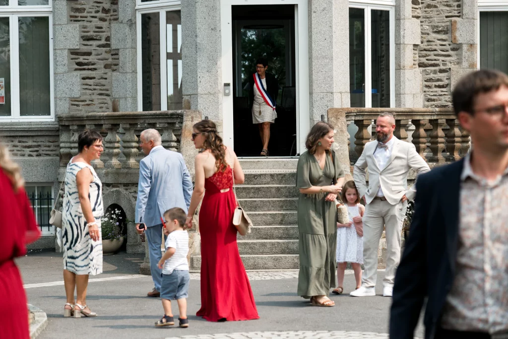 Invités de mariage devant la mairie de Saint-Hilaire-du-Harcouët en Normandie, style documentaire.