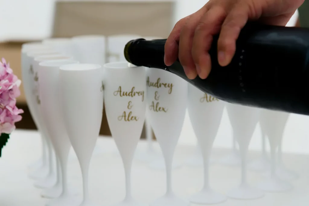 Main versant du champagne dans des flûtes blanches marquées Audrey et Alex pour un mariage en Normandie.