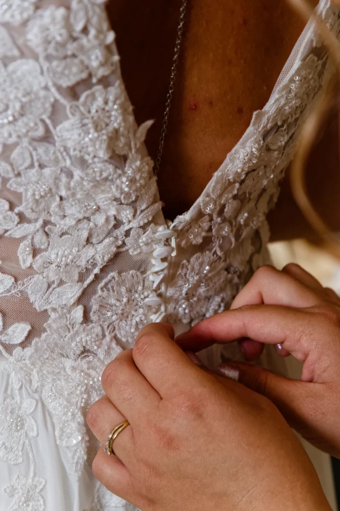 Mains ajustant les boutons d'une robe de mariée en dentelle à Saint-Hilaire-du-Harcouët, Normandie.