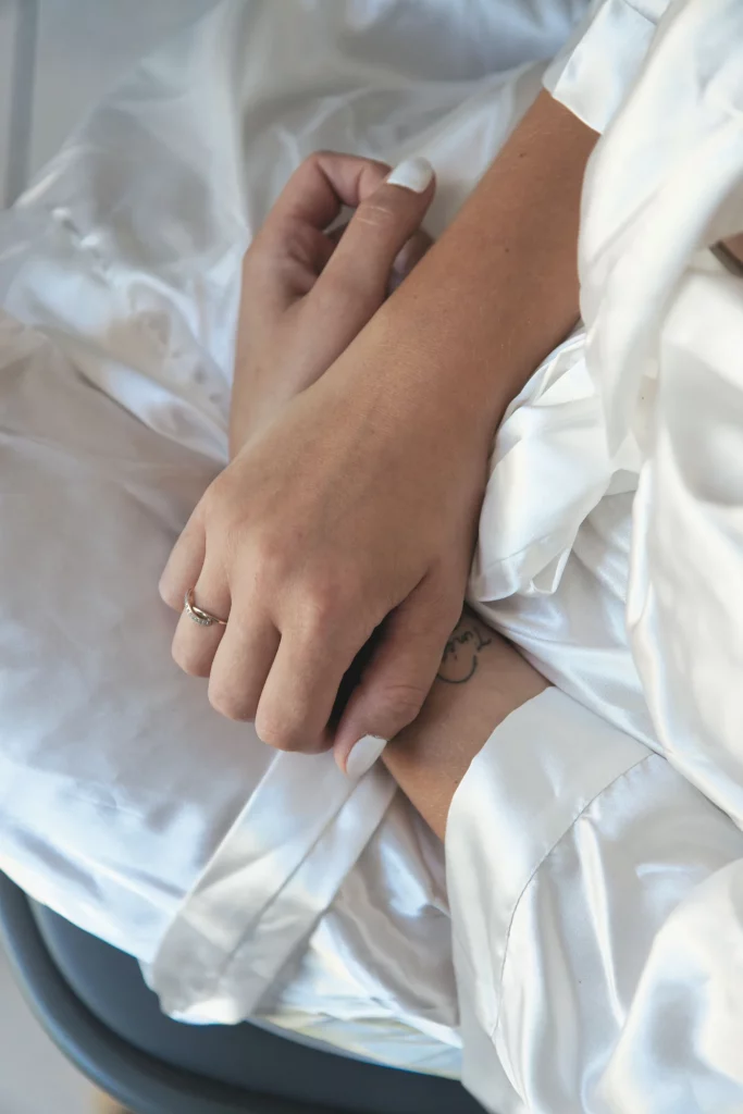 Mains d'une mariée sur sa robe en satin blanc, préparatifs à Saint-Hilaire-du-Harcouët, Normandie.