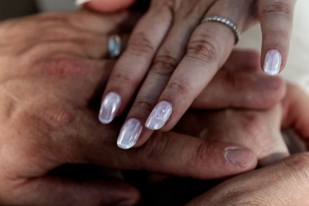 Mains des mariés entrelacées, manucure 'Oui' et alliances à Saint-Hilaire-du-Harcouët en Normandie.