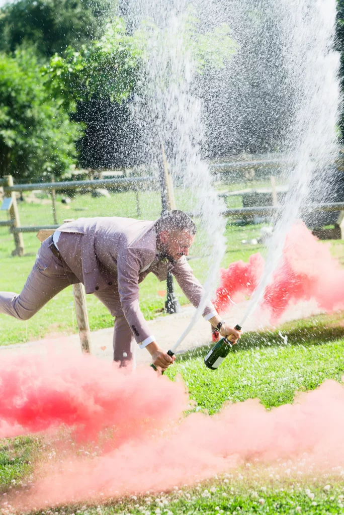 Le marié célébrant avec une bouteille de champagne et des fumigènes rouges en extérieur.