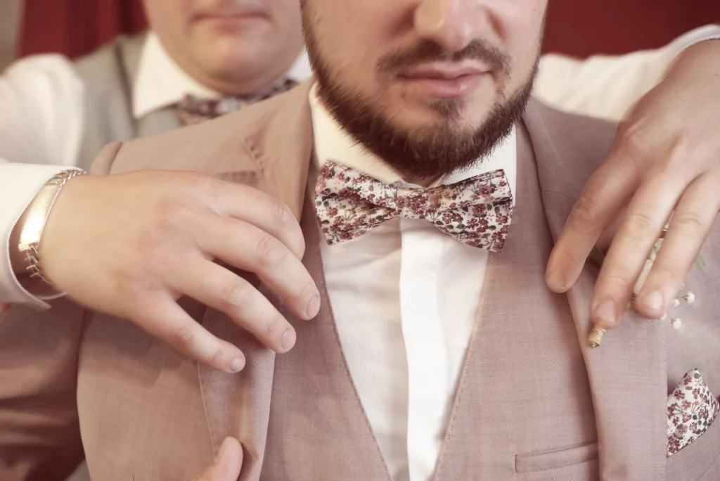 Marié en costume rose et nœud papillon fleuri ajusté à Saint-Hilaire-du-Harcouët, Normandie.