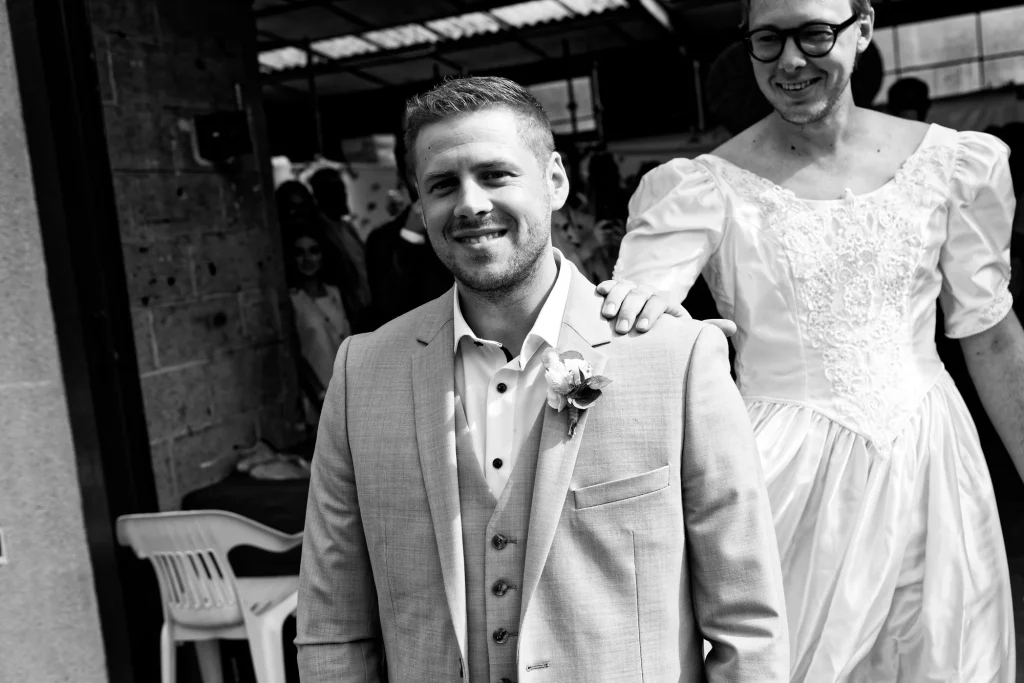 Marié souriant en Normandie surpris par un ami en robe de mariée, moment drôle et spontané.