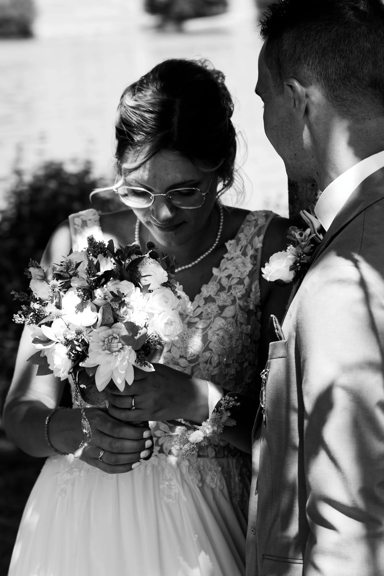 Mariée à lunettes admirant son bouquet en noir et blanc, mariage en Normandie.