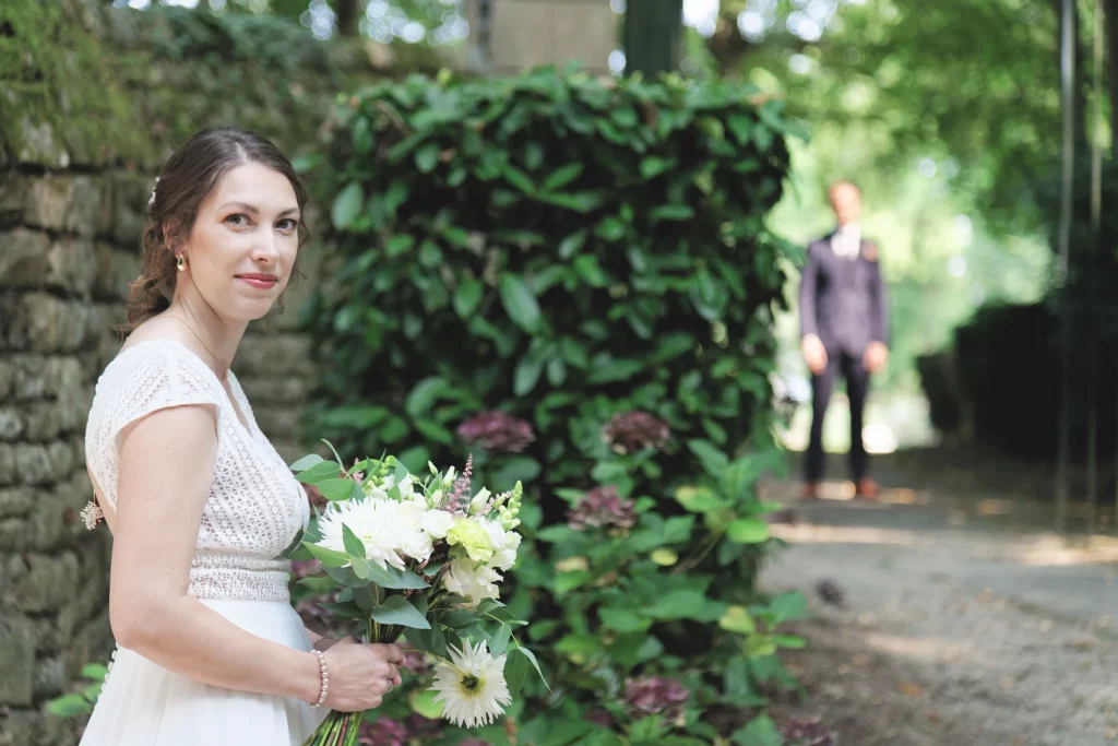 Mariée avec bouquet blanc au premier plan, marié flou en arrière-plan à Saint-Hilaire-du-Harcouët en Normandie.
