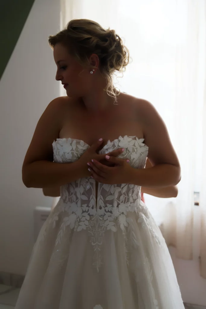 Mariée blonde ajustant sa robe en dentelle à Saint-Hilaire-du-Harcouët, Normandie.