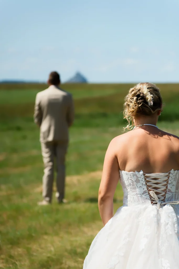 Mariée de dos devant le marié et le Mont Saint-Michel en Normandie pour leur premier regard.