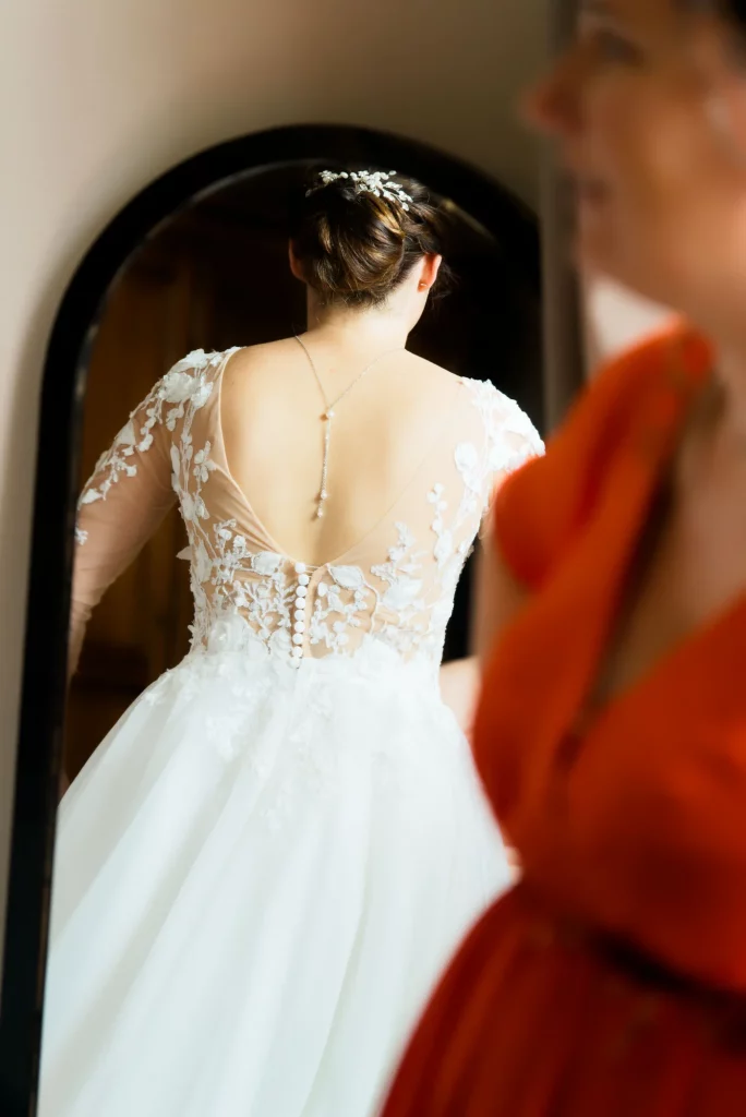 Mariée de dos devant son miroir avec collier de dos à Saint-Hilaire-du-Harcouët, Normandie.