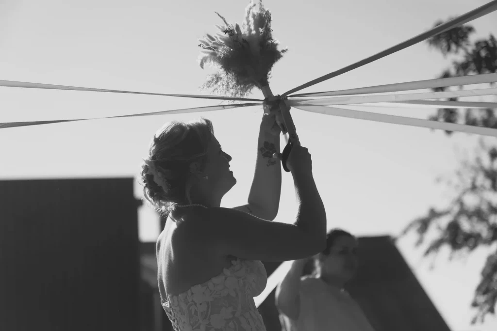 Mariée en Normandie coupant les rubans de son bouquet lors d'une cérémonie en plein air à Harcouët.