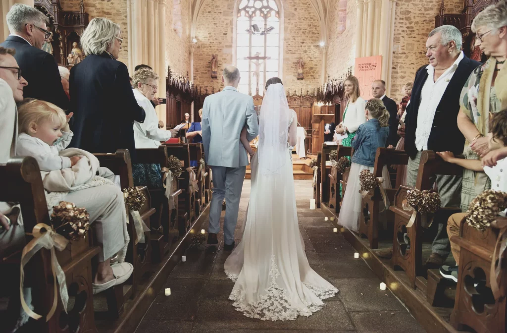 Mariée en robe blanche remonte l'allée d'une église en Normandie entourée de ses invités.