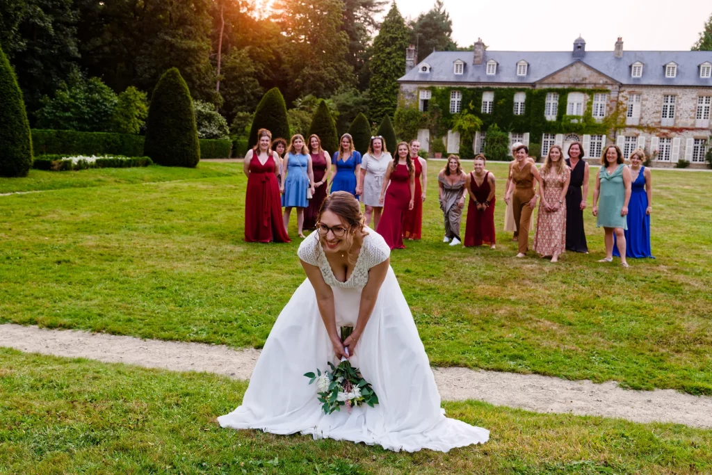 Mariée penchée avec bouquet devant ses amies au château de l'Harcouët en Normandie.