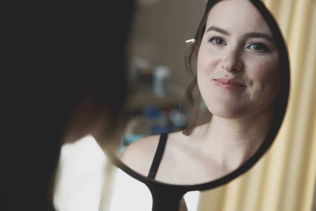 Mariée souriante admirant son reflet dans un miroir rond lors des préparatifs à Saint-Hilaire-du-Harcouët.