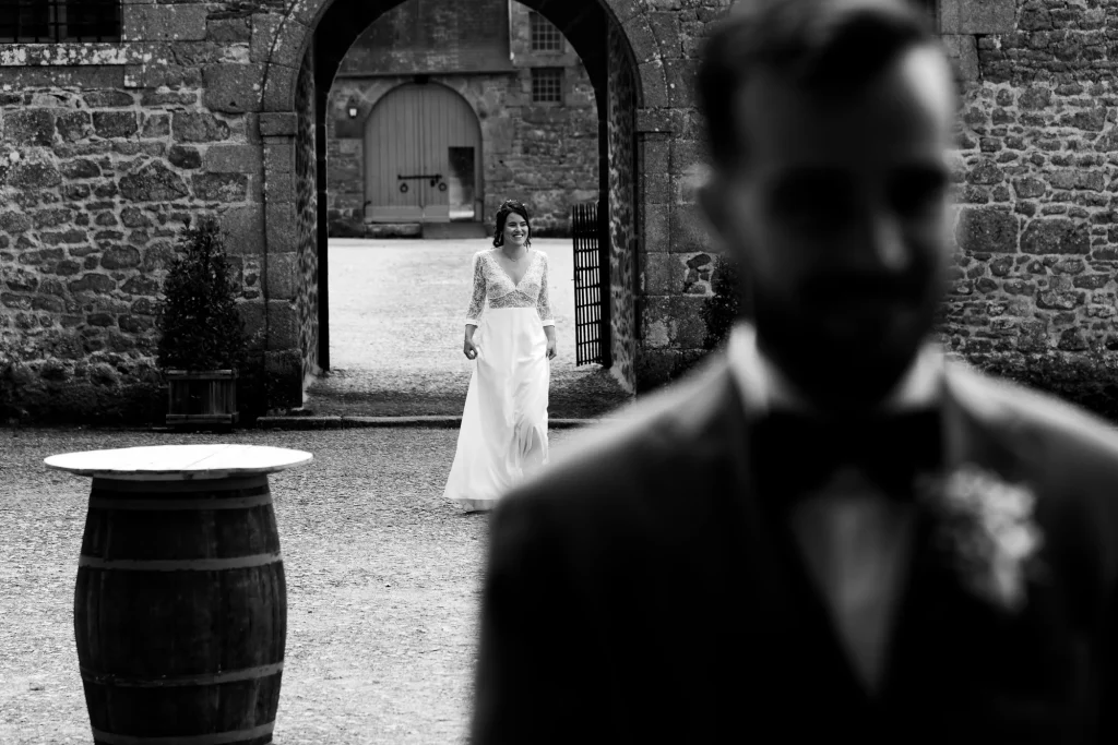 Mariée souriante marchant vers le marié sous une arche en pierre en Normandie.