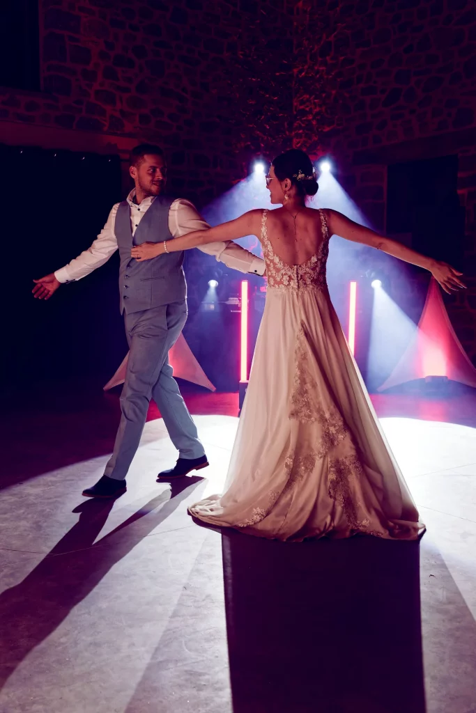 Mariés dansant l'ouverture de bal à Saint-Hilaire-du-Harcouët, robe dentelle et costume bleu sous des projecteurs.