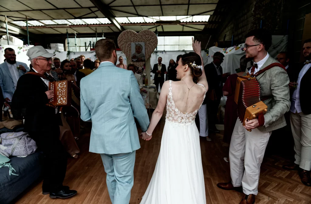 Mariés de dos marchant avec des accordéonistes à Saint-Hilaire-du-Harcouët, Normandie.