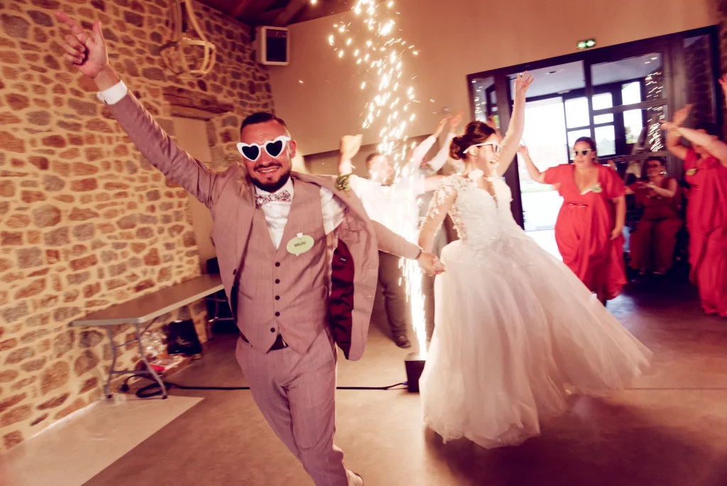 Entrée dynamique des mariés avec lunettes de soleil cœur et jets de scène étincelants.