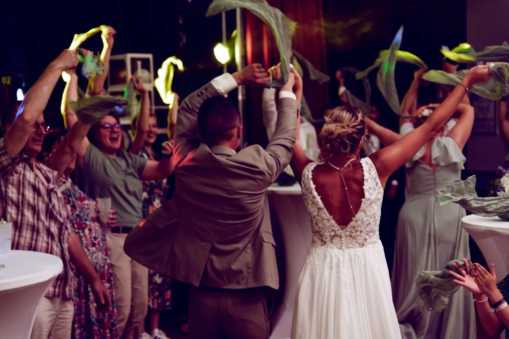 Mariés et invités dansant à Saint-Hilaire-du-Harcouët, Normandie, agitant des tissus verts en l'air.