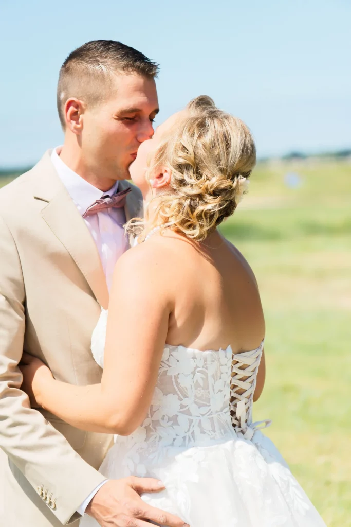 Mariés s'embrassant dans un champ en Normandie, robe dentelle et costume beige à Saint-Hilaire-du-Harcouët.