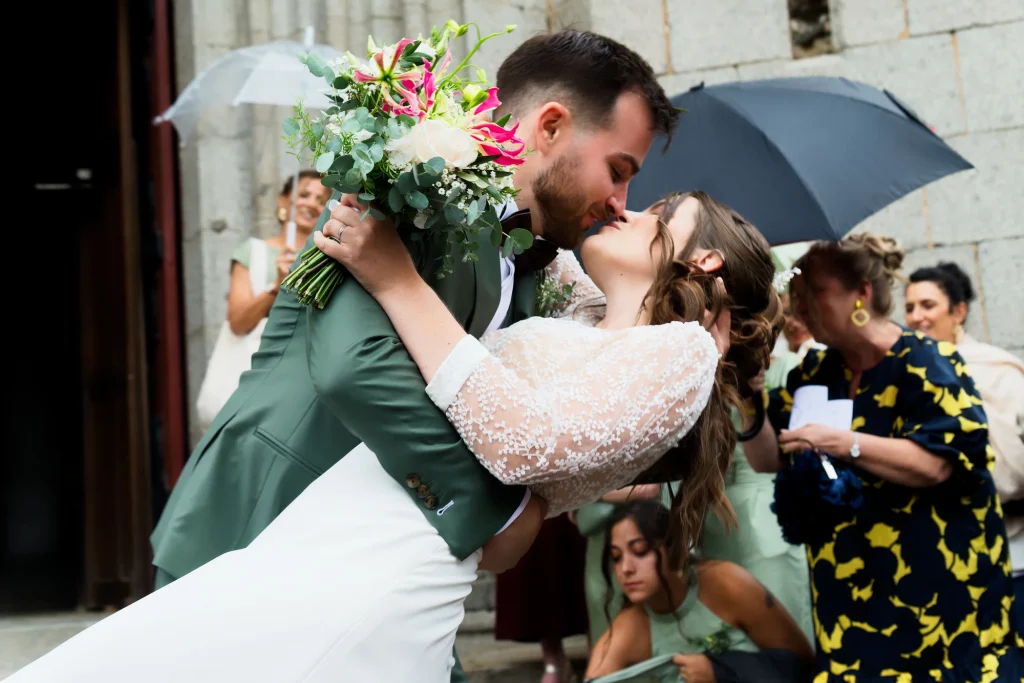 Mariés s'embrassant en Normandie, robe dentelle et costume vert sous les parapluies à Saint-Hilaire.