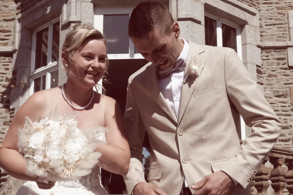 Mariés souriants sortant de la mairie à Saint-Hilaire-du-Harcouët en Normandie avec bouquet de roses blanches.