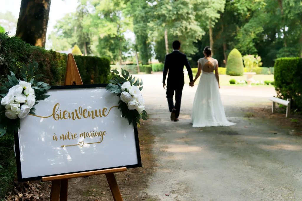 Panneau de bienvenue doré mariage Normandie avec couple de mariés flous marchant dans un parc à Avranches.
