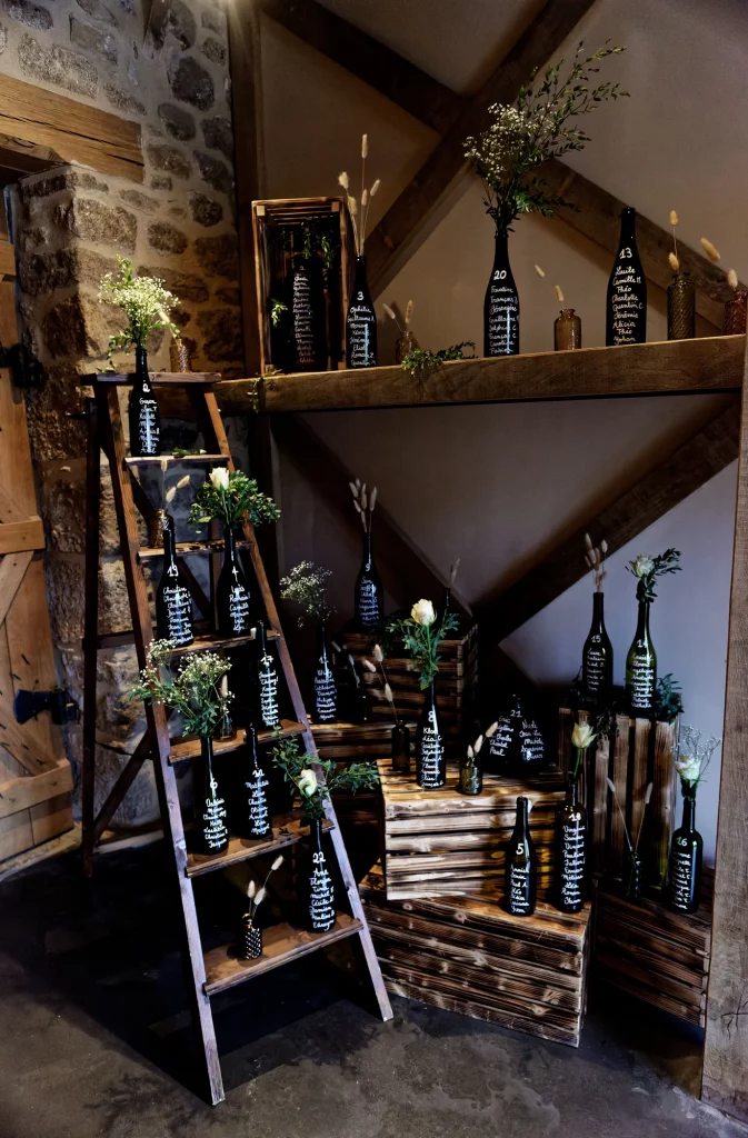 Plan de table original : bouteilles noires calligraphiées sur échelle en bois, mariage en Normandie.