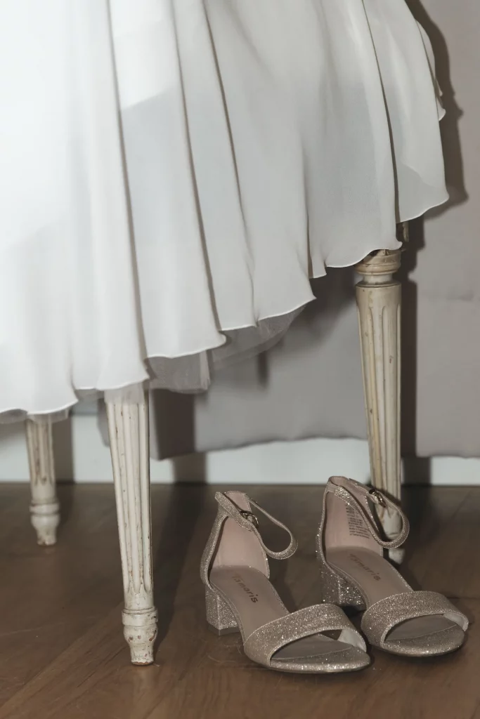 Robe de mariée blanche sur chaise vintage et chaussures dorées pailletées, mariage en Normandie.