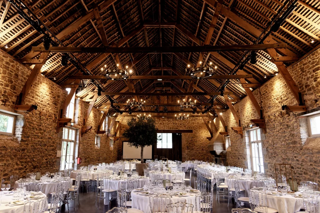Salle de réception de mariage dans une grange en pierre avec poutres apparentes à Saint-Hilaire-du-Harcouët.