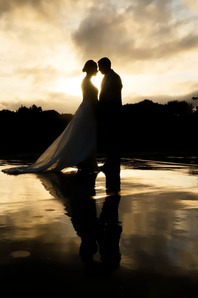 Silhouette de mariés au coucher de soleil avec reflet sur sol mouillé près d'Avranches en Normandie.