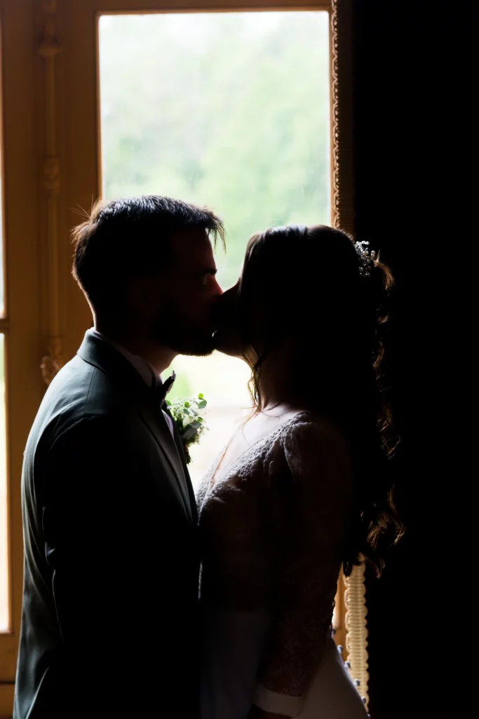 Silhouette de mariés s'embrassant devant une fenêtre en Normandie. Style cinématographique et romantique.