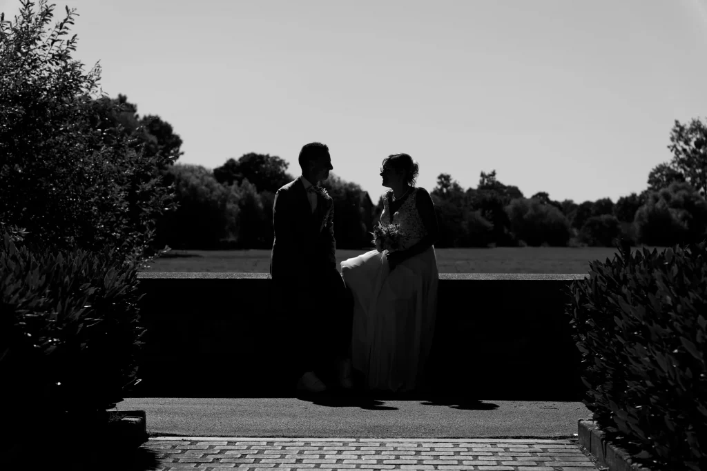 Silhouette noir et blanc d'un couple de mariés assis sur un muret en Normandie à Saint-Hilaire-du-Harcouët.
