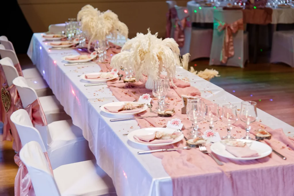 Table de mariage décorée en Normandie avec chemin de table vieux rose, pampas blanches et vaisselle élégante.